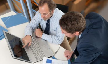 Two men sitting at a table looking at a laptop.